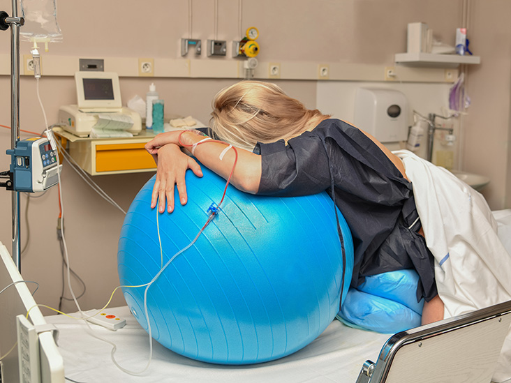 A woman in labour leaning against a birthing ball