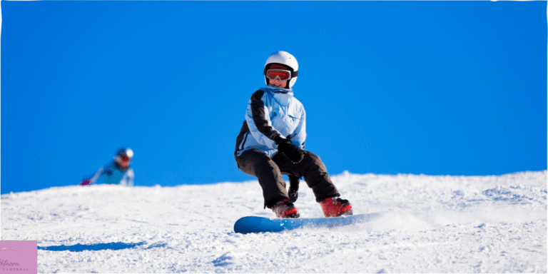 A young child snowboarding down a mountain with blue skies behind them. Source: Canva