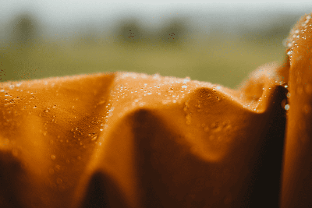 An orange rain jacket with rain droplets on it. Photo by Claudio Schwarz on Unsplash