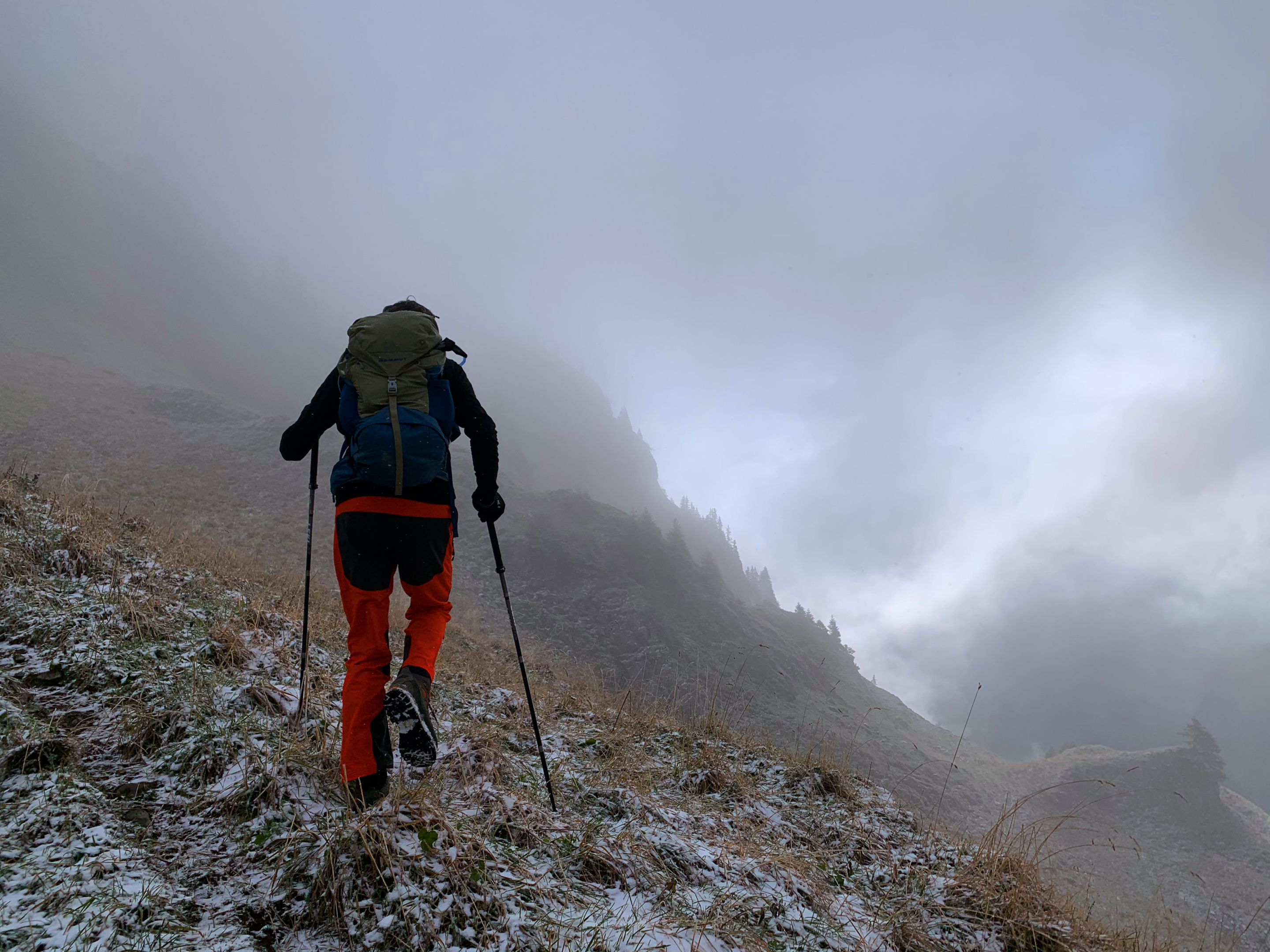 A hiker in misty conditions using walking poles to cross icy terrain. Photo by Stéphane Fellay on Unsplash