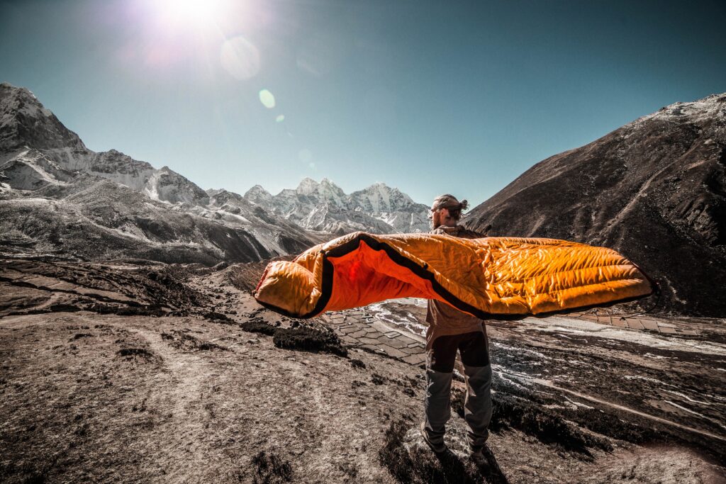 Someone holding their sleeping bag in the breeze up a mountain. Photo by Martin Jernberg on Unsplash