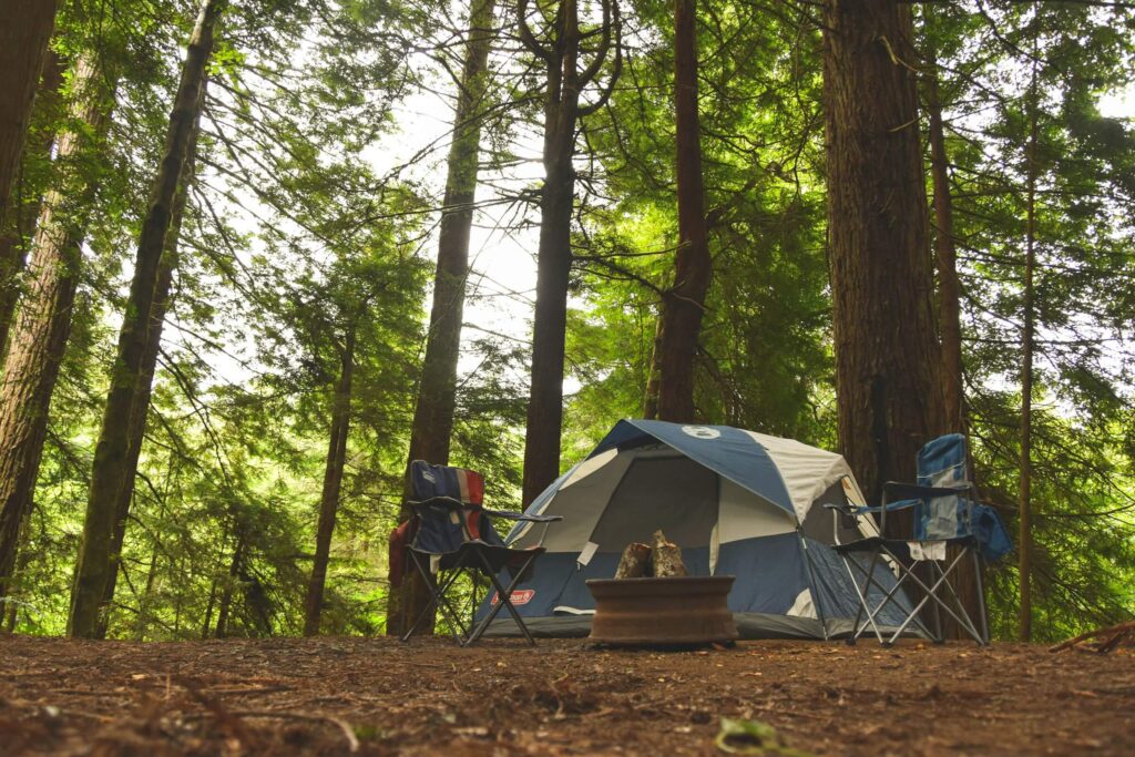 A tent with chairs outside of it in the woods. Photo by Everett McIntire on Unsplash