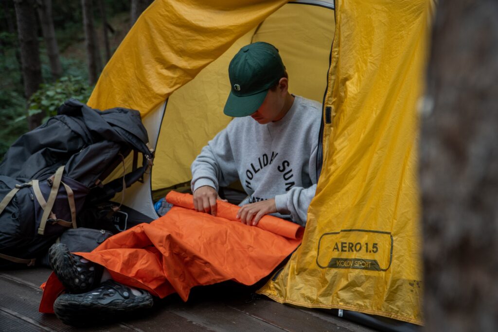 A man sitting in a tent folding up a sleeping mat. Photo by Chaewul Kim on Unsplash