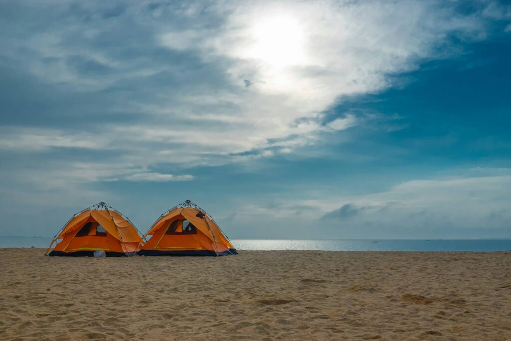 Two orange tents on a beach, facing the sea. Photo by Katsu Utaharu on Unsplash
