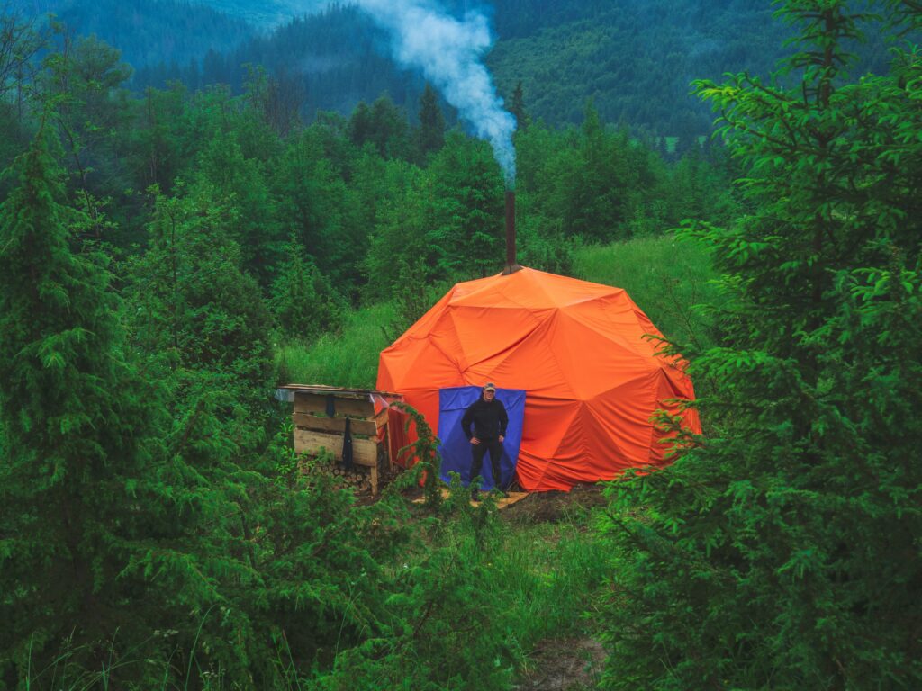 An orange hexagon shape tent in a lush green forest. Photo by Michael Walk on Unsplash