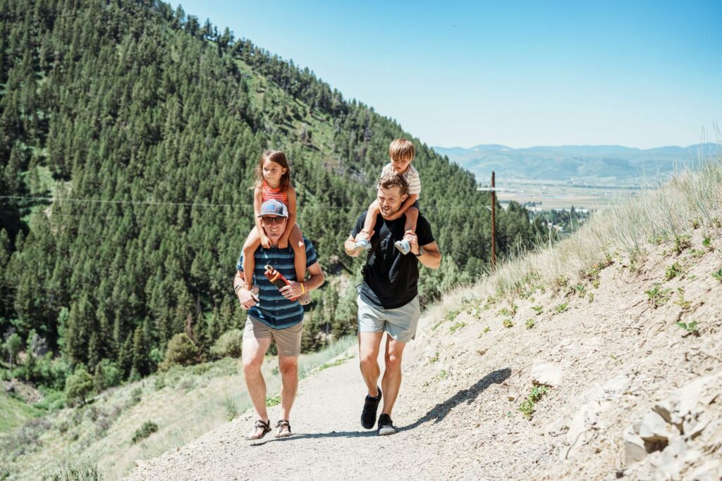 Two men hiking with two young children on their shoulders. Photo by Land O'Lakes, Inc. on Unsplash