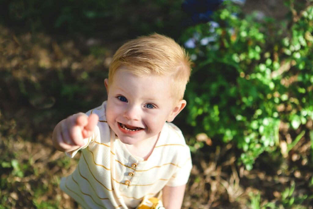 A happy, smiling, little boy of about 2-years-old, pointing up at the camera. Photo by Philip White on Unsplash
