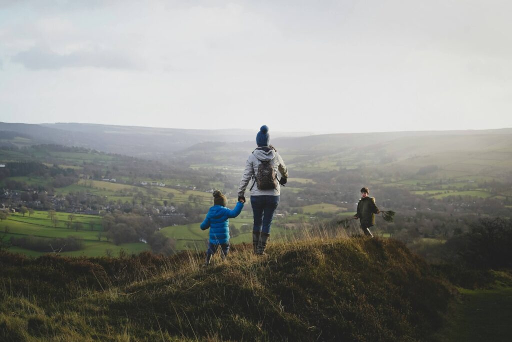 A mum hiking with two young children over hills with a valley below them. Family hiking in the UK. Photo by BEN ELLIOTT on Unsplash