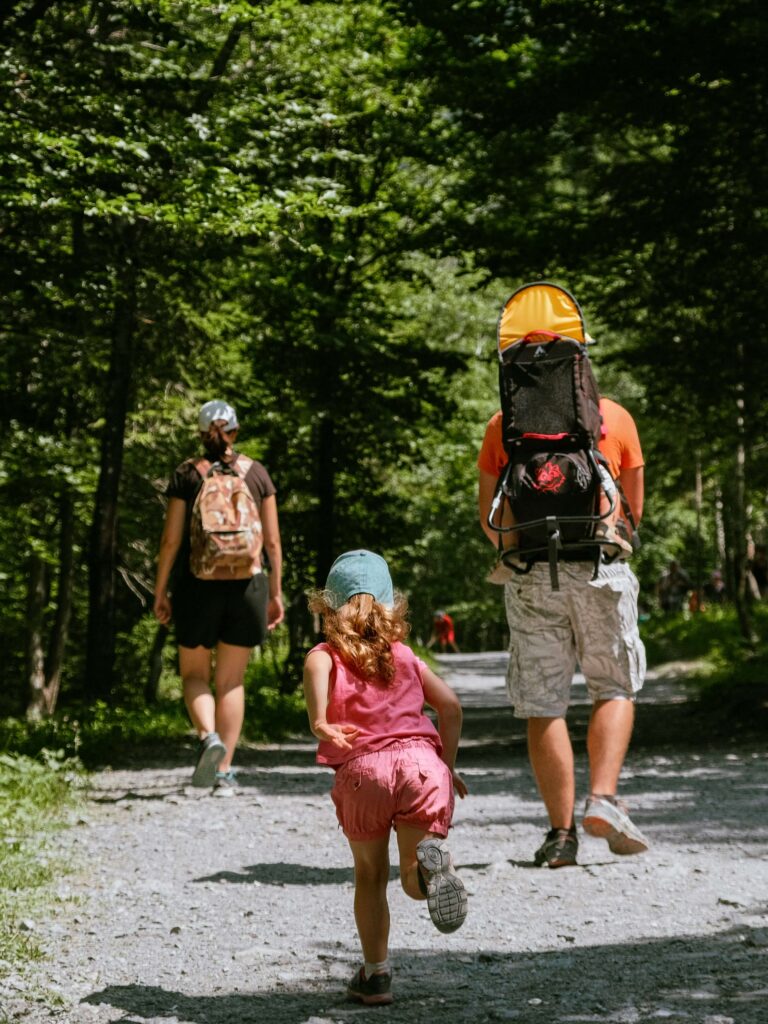 A toddler running behind her parents walking along a gravel forest path. Photo by Christian Harb on Unsplash
