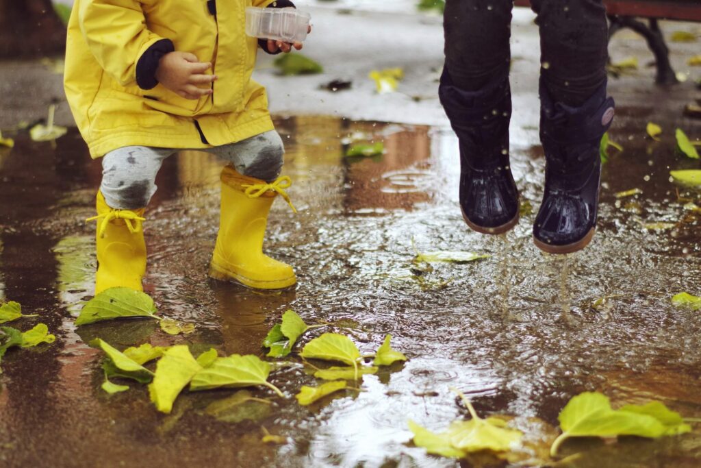 Young children jumping in puddles with wellies on. Camping in the rain activities for families. Photo by Xavi Cabrera on Unsplash