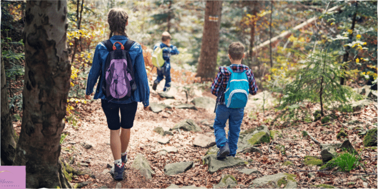 Young children with backpacks on, walking through a wooded area. Source: Canva