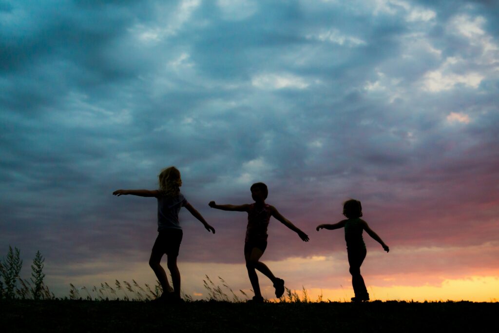 Three young children playing outside in the fading light. Photo by Jess Zoerb on Unsplash