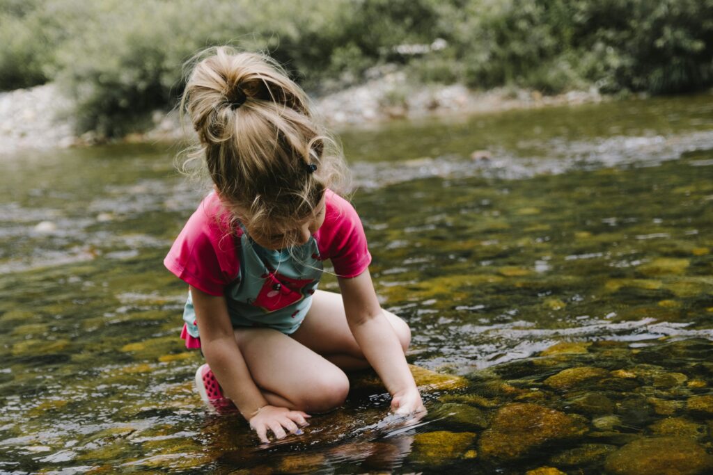 A child trying to catch something while kneeling in a stream. Photo by Kelly Sikkema on Unsplash