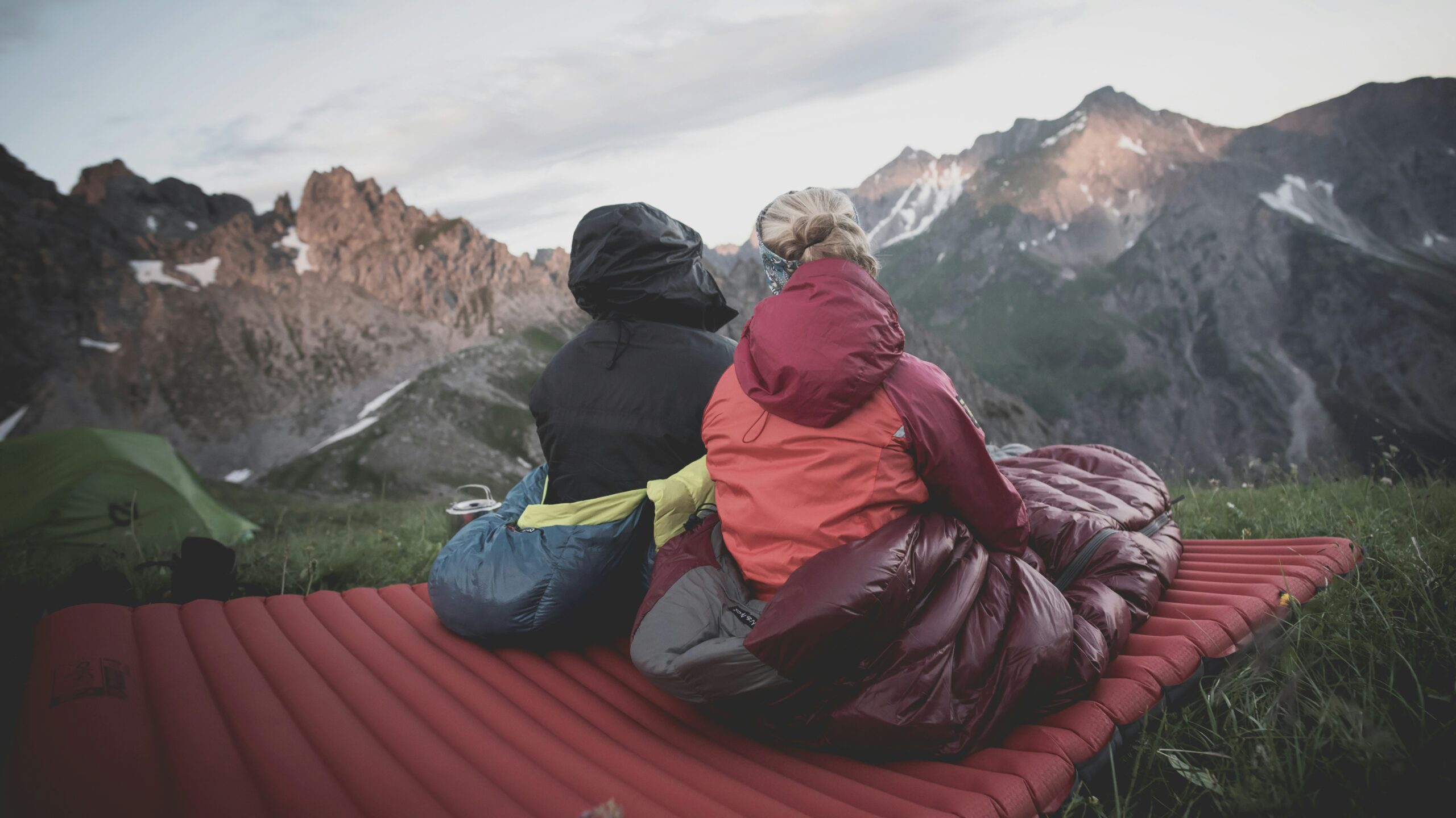 Two people sitting in their sleeping bags overlooking mountains. Photo by Lucas Canino on Unsplash