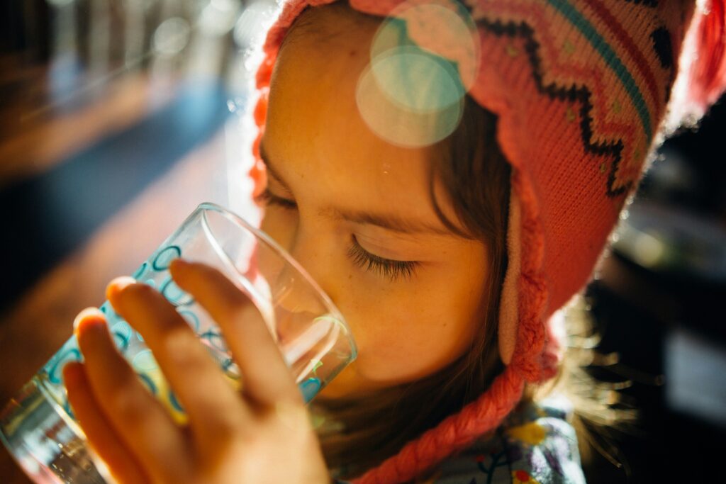 A little girl drinking from a glass. Photo by Johnny McClung on Unsplash