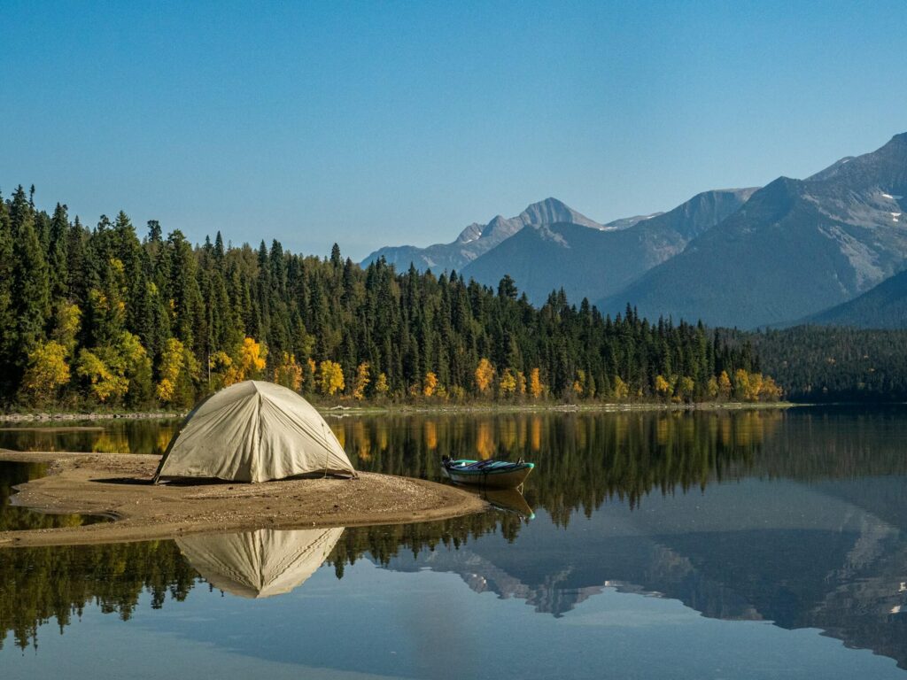 A tent next to water with trees and mountains in the background. Photo by Lesly Derksen on Unsplash