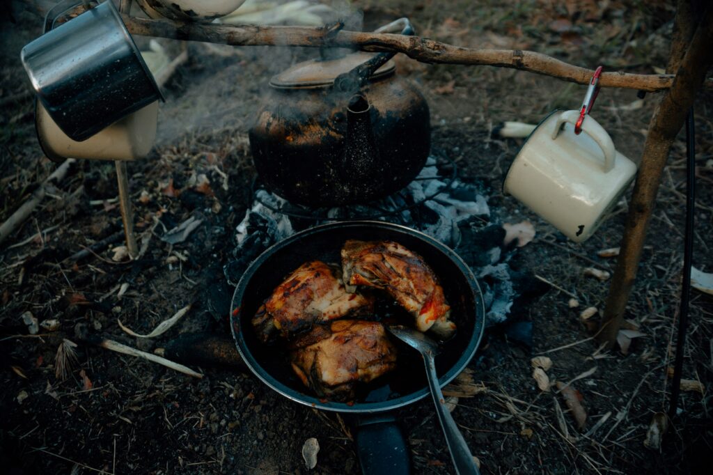 Food being cooked outside with a camping kettle and two camping mugs nearby. Photo by Angga Kurniawan on Unsplash