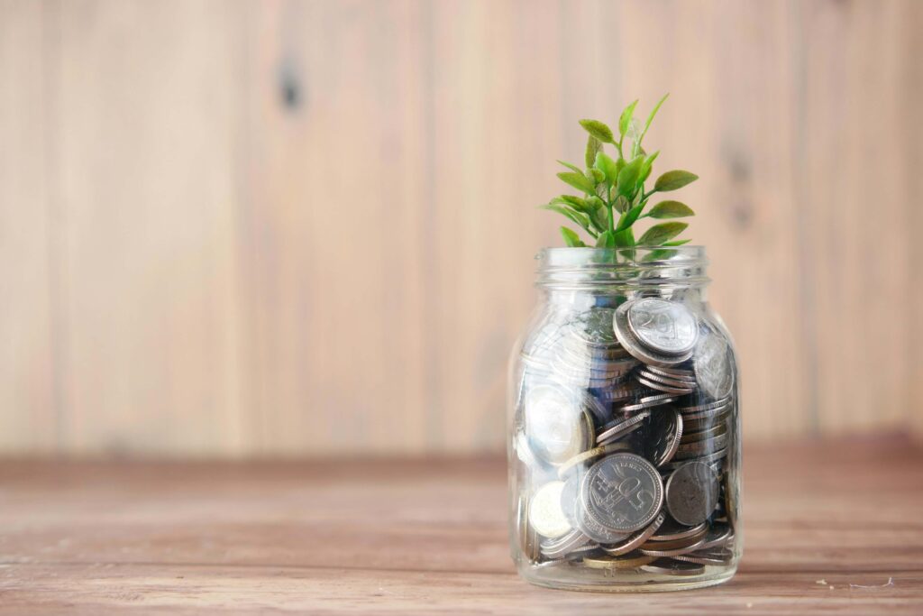A glass jar with money in it and a plant growing out of the top. Photo by Towfiqu barbhuiya on Unsplash