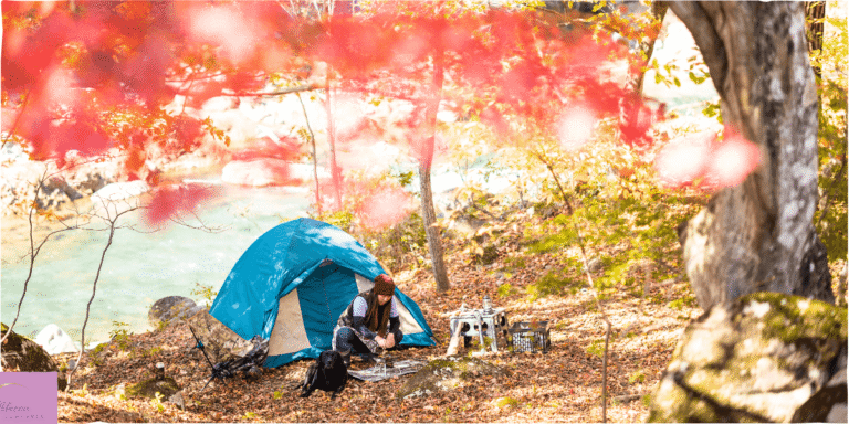 Someone camping in the woods with the leaves on some trees turning red. Source: Canva