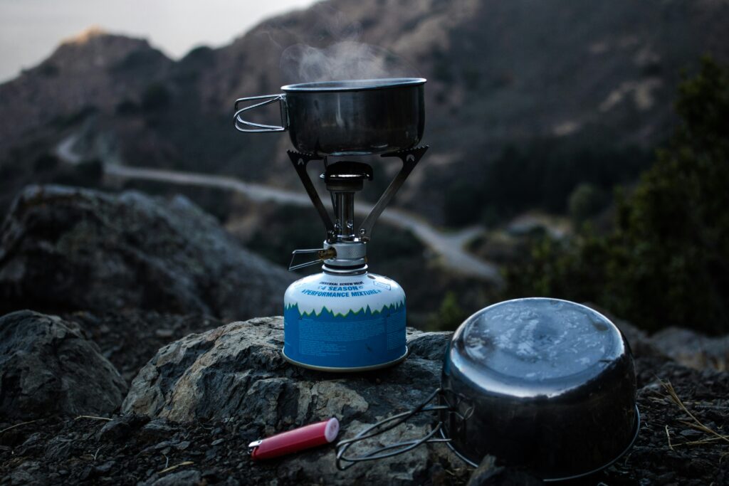 A camping stove heating a pot on some rocks. Best camping stoves on a budget. Photo by Sage Friedman on Unsplash