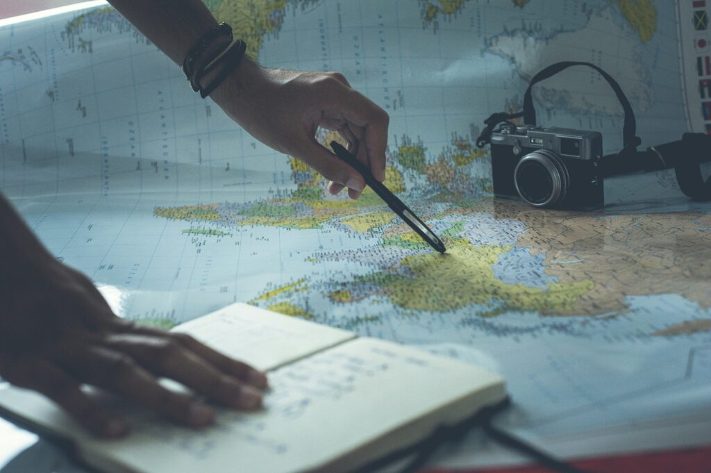Someone pointing on a map with a pen with a camera on it. Photo by Glenn Carstens-Peters on Unsplash