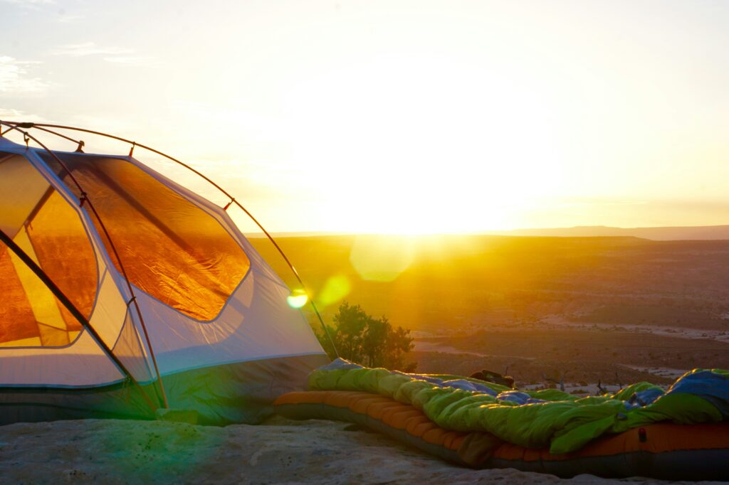 A tent and a sleeping bag in the sunrise. How to keep warm in a tent. Photo by Jack Sloop on Unsplash