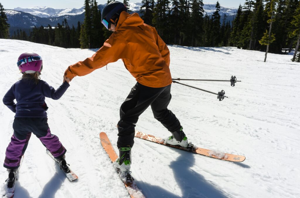 Someone teaching a child to ski. Skiing with kids. Photo by Greg Rosenke on Unsplash