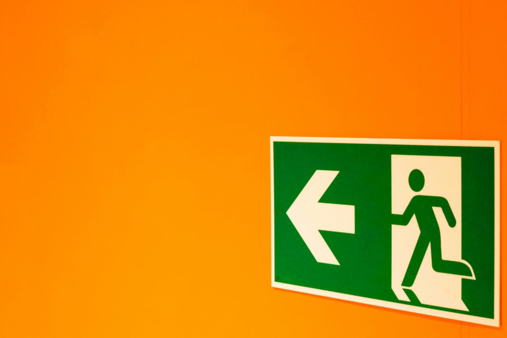A green exit sign on an orange wall. Photo by DDP on Unsplash