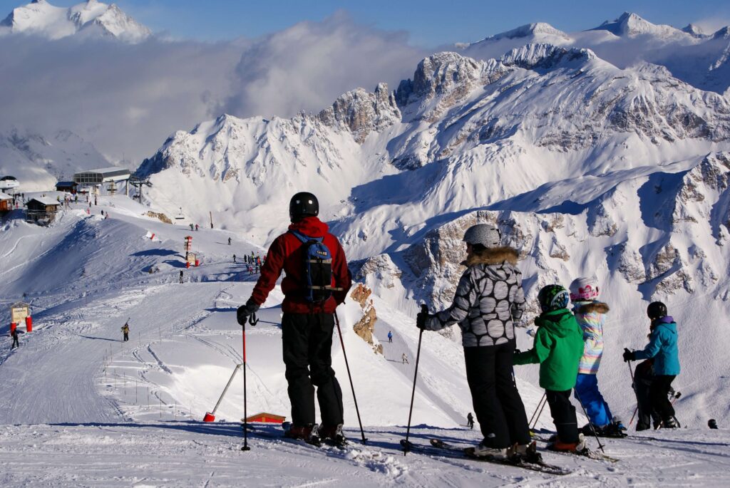 A family skiing together, looking at the mountain at the top of a run. Budget family ski resorts in France. 