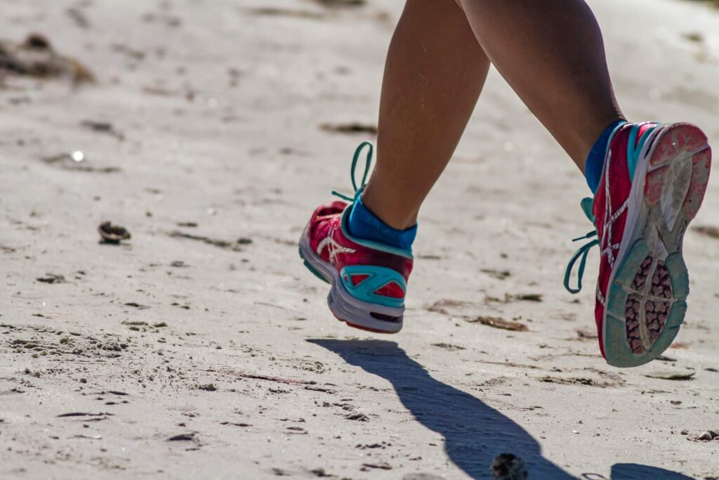 A close up of someone running on the sand, showing just the person's running trainers. Photo by Dulcey Lima on Unsplash