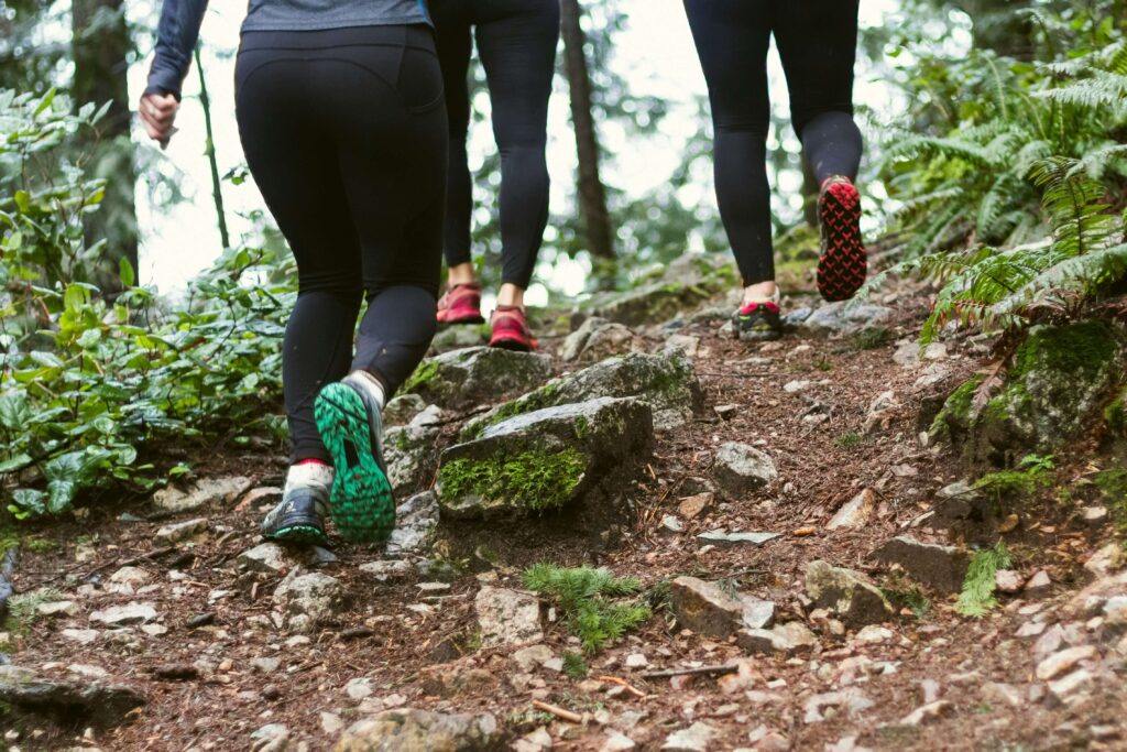 Three trail runners going uphill through a forested path. Photo by Greg Rosenke on Unsplash
