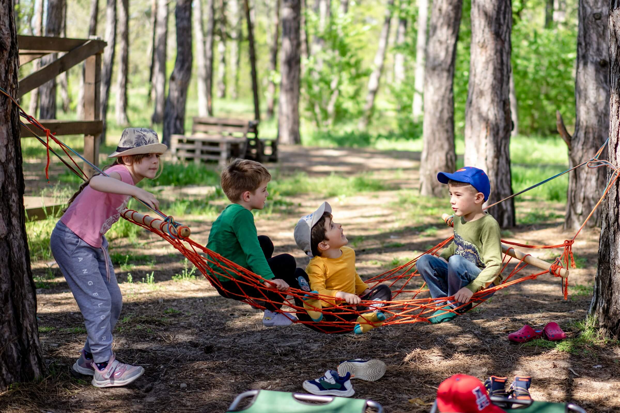 Four children swinging and sitting on a rope hammock outside among the trees. Photo by Alexandr Podvalny on Unsplash