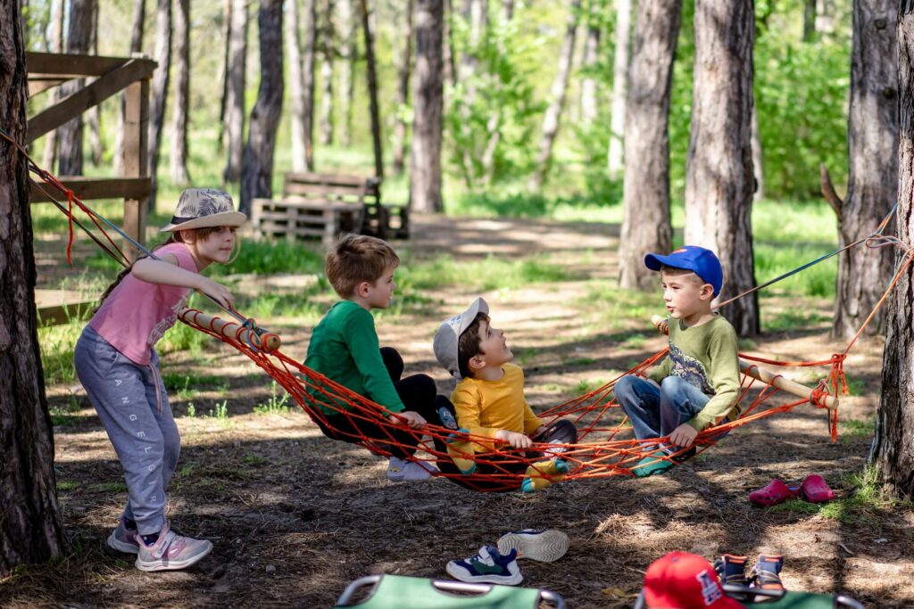 Three boys and one girl playing outside on a rope hammock. Photo by Alexandr Podvalny on Unsplash