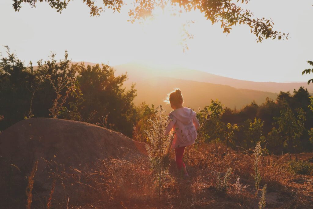 A young child walking through flower bushes in the evening sun. Summer camping activities for kids. Photo by Yunus Emre Öztürk on Unsplash