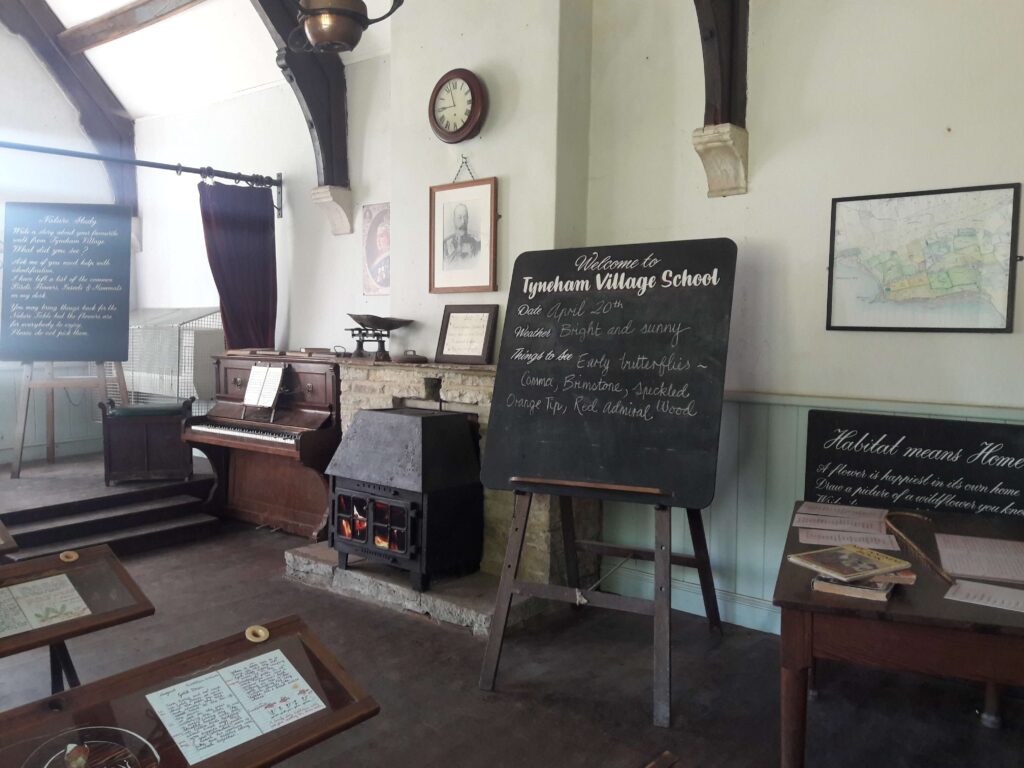 Inside the school at Tyneham Village where you can see a blackboard, an old piano, a non-working fireplace, rows of tables, and bookcases. Source: Rebecca Campbell Ltd