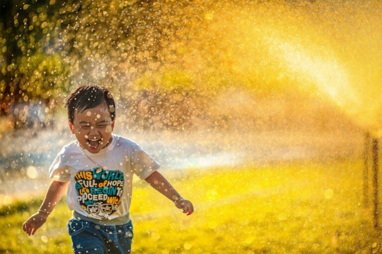 A little boy running through a water spray in hot weather. How to keep kids cool camping in hot weather. Photo by MI PHAM on Unsplash