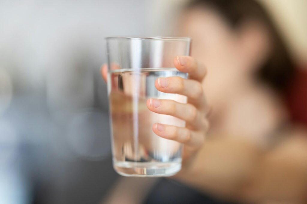 Someone holding a glass of water. How to keep kids cool camping in hot weather. Photo by engin akyurt on Unsplash