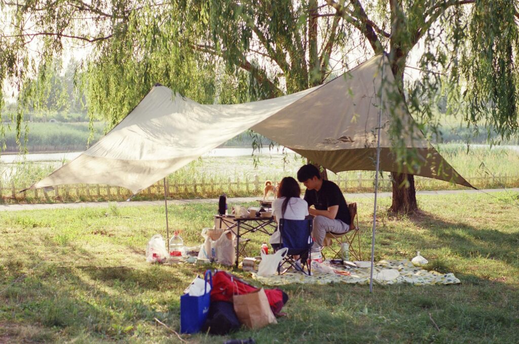 People sitting under a canopy for shade against the sun. Hot weather camping with kids. Photo by Austin on Unsplash