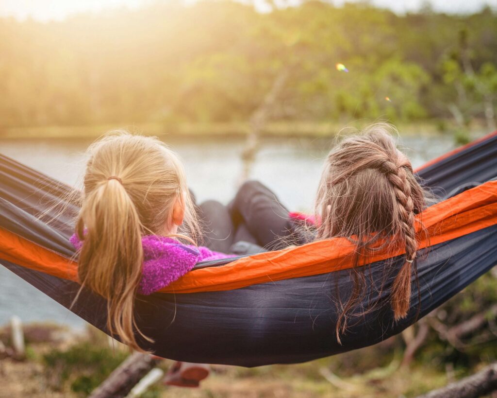 Two girls resting on a hammock. Camping with kids. Photo by 🇸🇮 Janko Ferlič on Unsplash