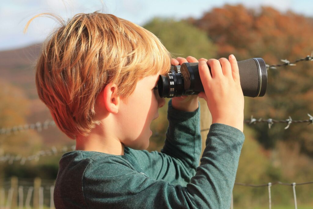 A little boy looking through binoculars outside. Hiking games for kids. Photo by David Carpenter on Unsplash